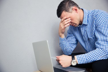 Man with head in hand holding credit card looking at laptop