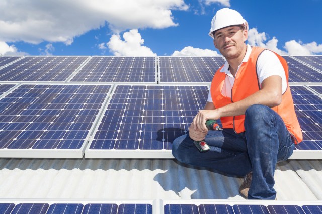 Man in orange vest and white hard hat sits near new solar panels
