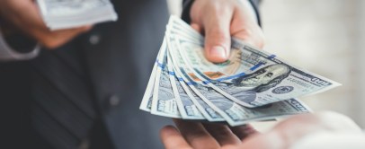 Close-up of a person handing a stack of $100 bills to another person, representing a short-term or emergency cash loan.